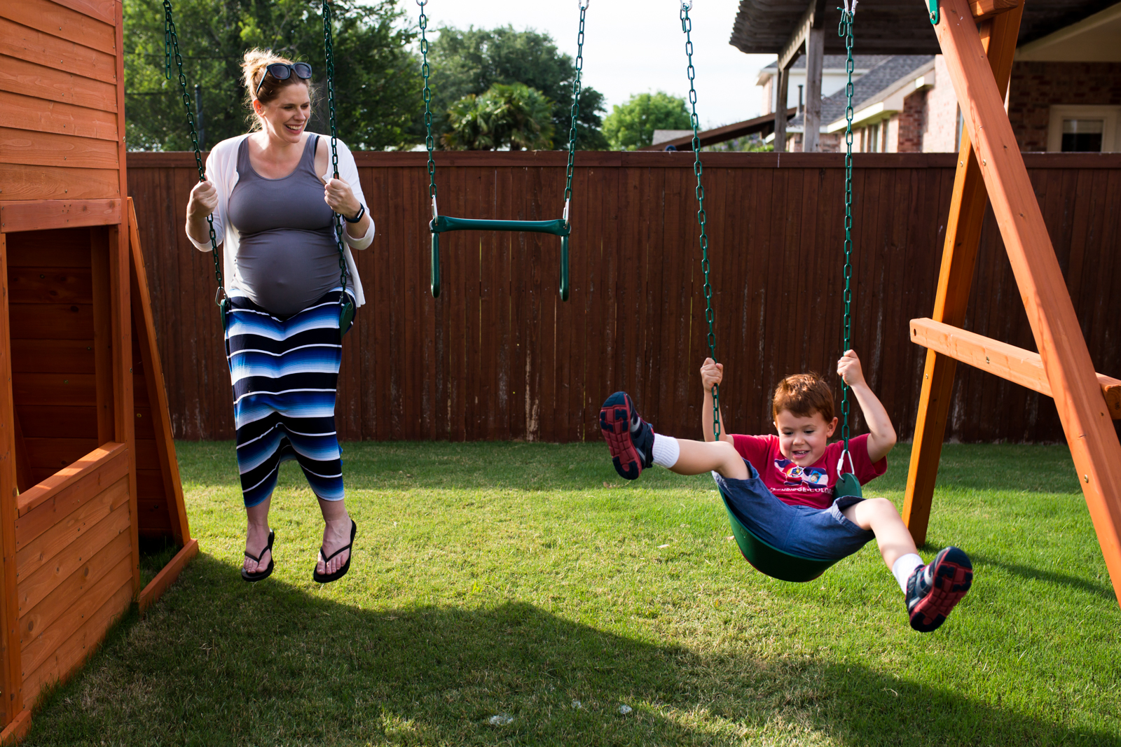 McKinney Maternity Photographer Lawren Rose Photography catches a great moment with her camera of a pregnant Mom and her redheaded son swinging on a swing set in their backyard