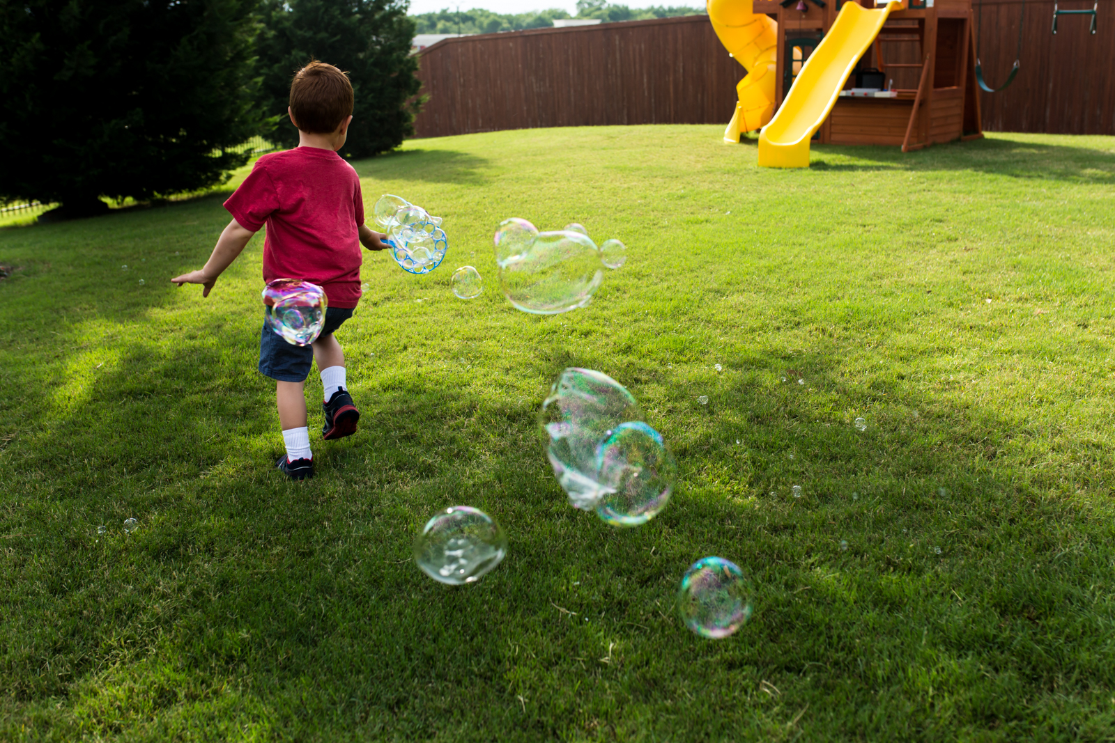Lawren Rose Photography captures a photo of a red headed little boy running in the bright green grass with giant bubbles flowing behind him in McKinney Texas