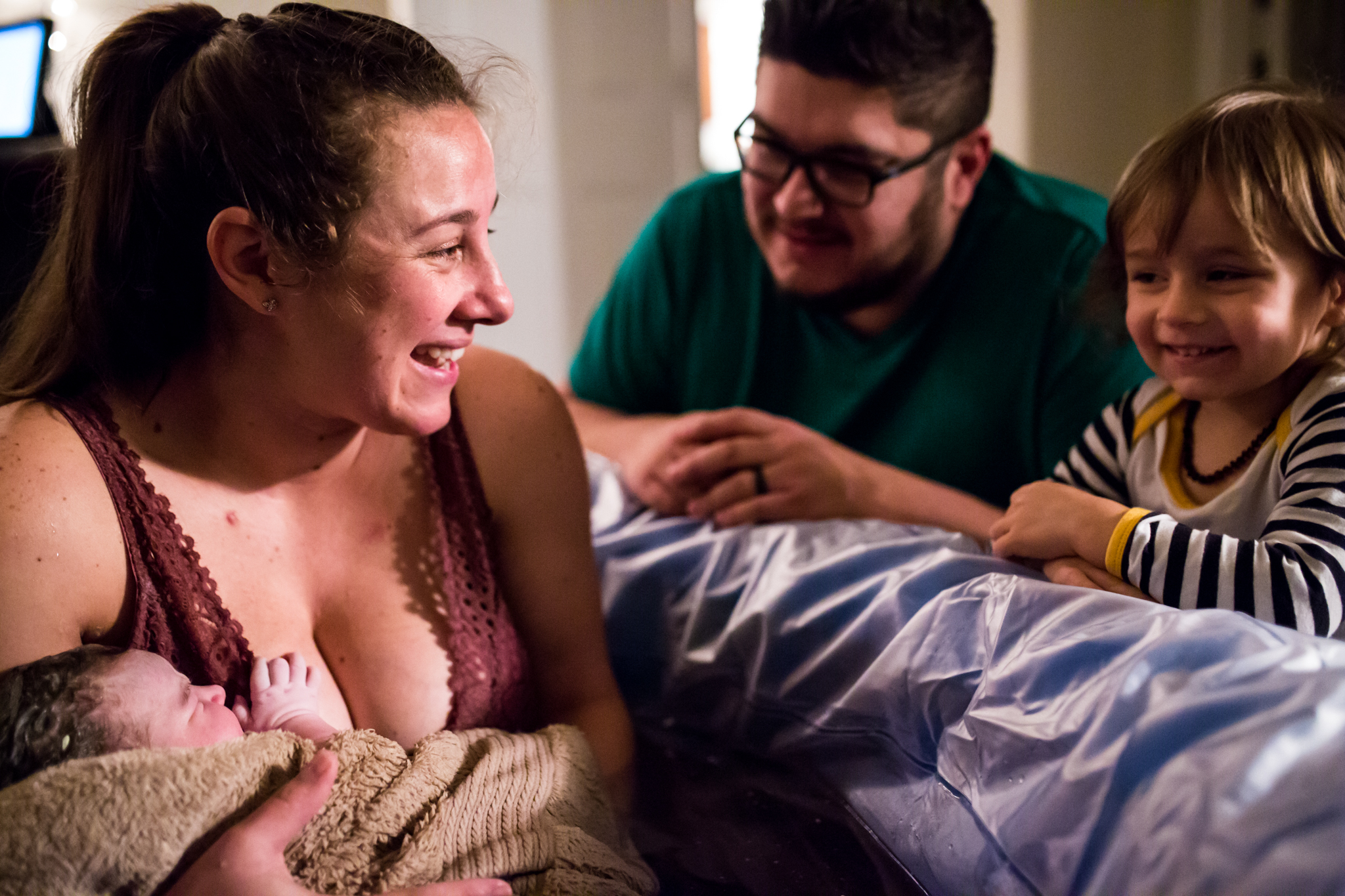 DFW Birth Photographer, Lawren Rose Photography, captures a moment when a Mom just has her newborn baby girl in a water birth at home, looking and gazing at her husband and son