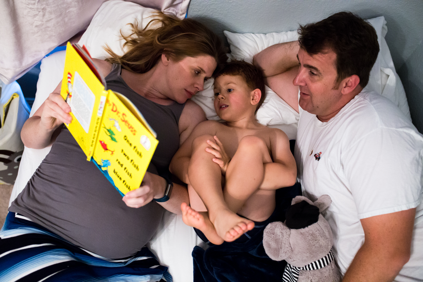 Maternity Photographer Lawren Rose Photography takes a photo from above of a family of 3 laying in bed reading a dr. seuss book in mckinney texas