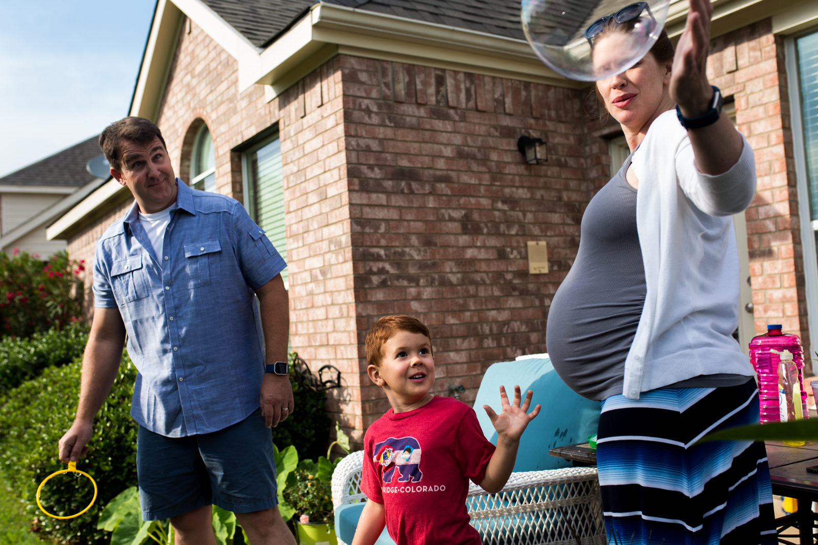 McKinney Photographer Lawren Rose Photography captures a photo of a family of 3 outside in their backyard blowing giant bubbles