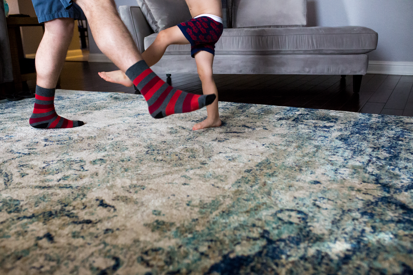 Lawren Rose Photography takes a minimalist photo of a dad and son dancing where dad is wearing funky socks on the living room floor in mckinney texas