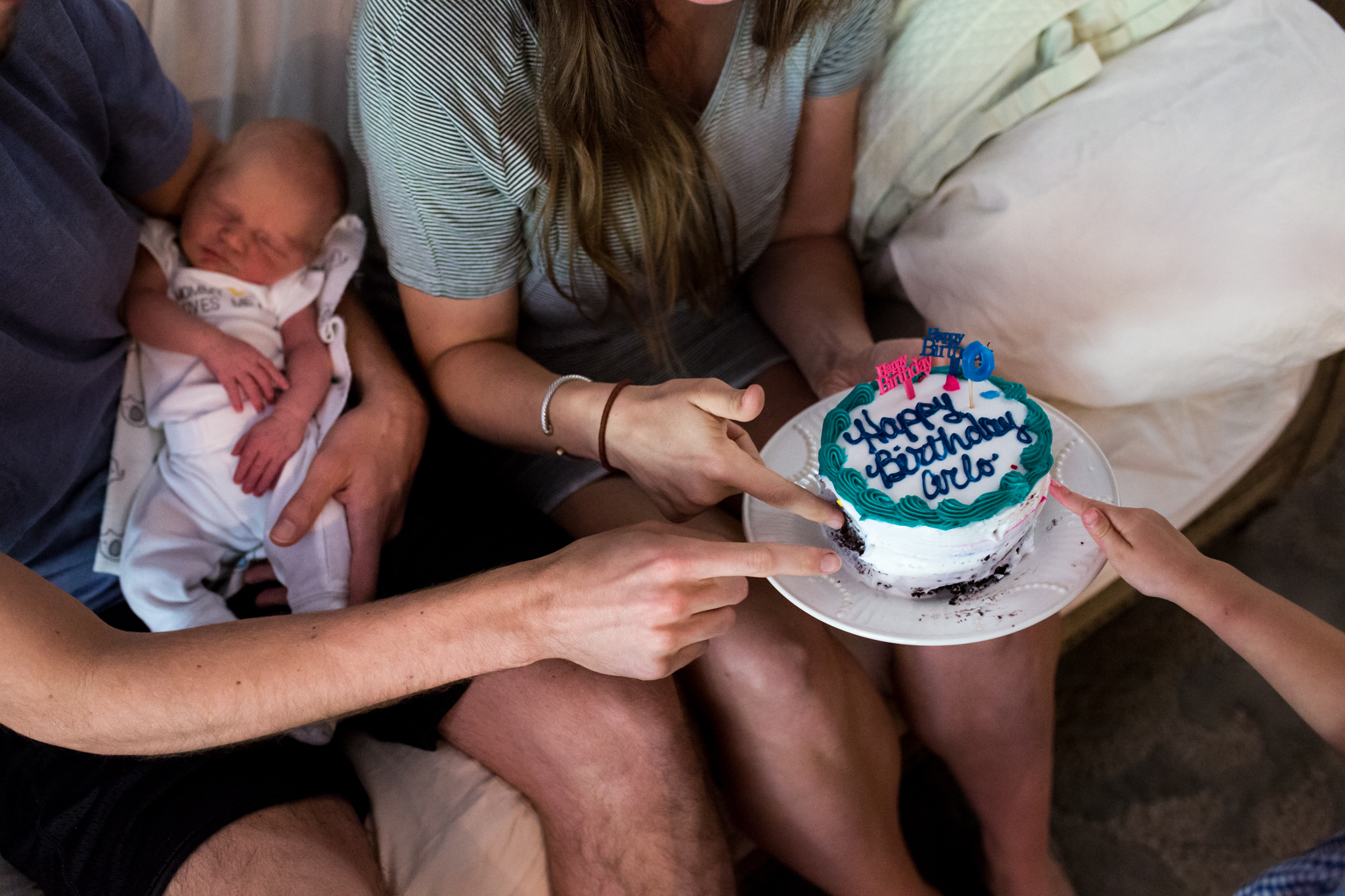 Lawren Rose Photography takes a picture of a family of 4 celebrating the birth of their new son Arlo. The picture shows 3 hands and fingers digging into a birthday cake while baby arlo lays nearby