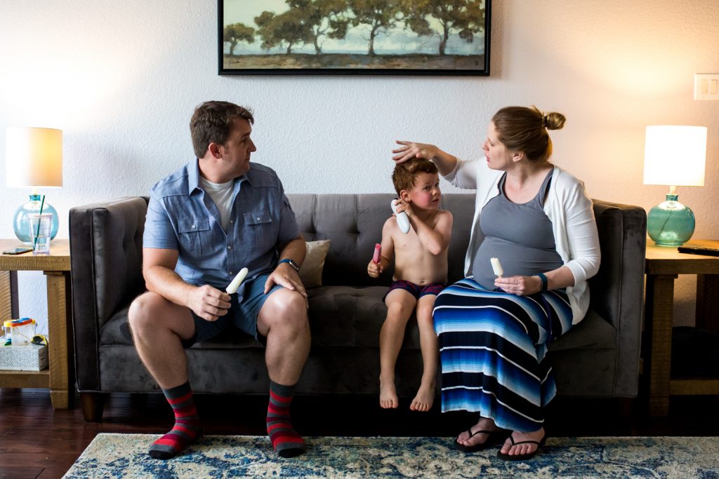 Lawren Rose Photography takes a family portrait of a pregnant Mom, Father, and their 4 year old son sitting on a couch eating popsicles in a McKinney Texas home