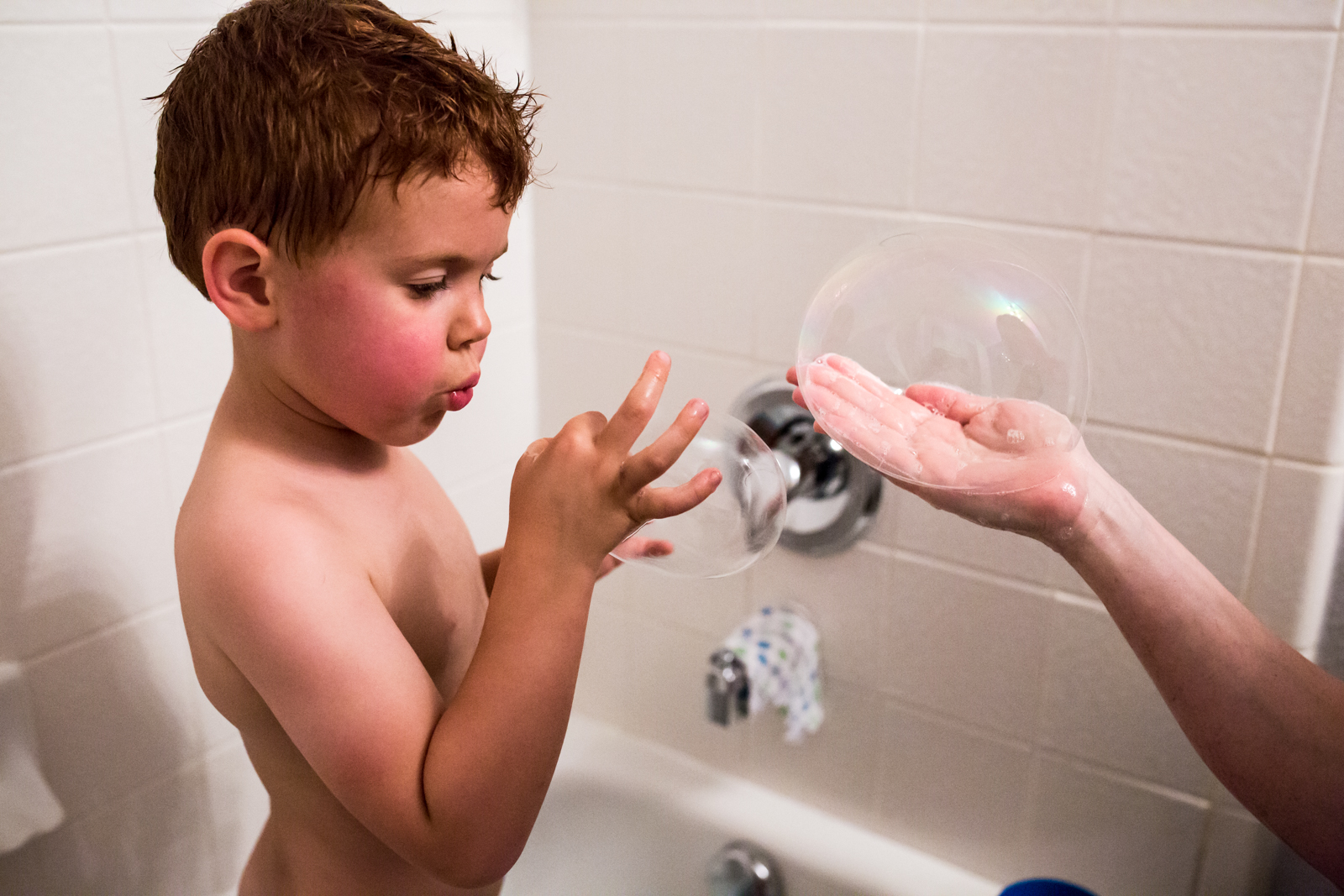 Lawren Rose Photography captures a special moment between a red headed boy and his mom blowing hand bubbles in the bathtub in McKinney Texas