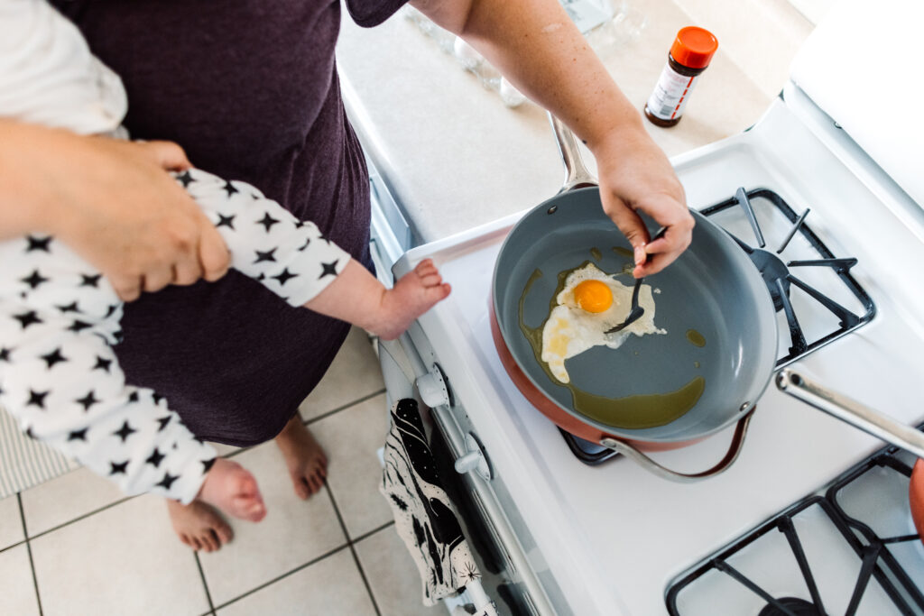 dallas documentary family photographer lawren rose photography takes a picture of a mom holding her 5 month old baby while cooking eggs