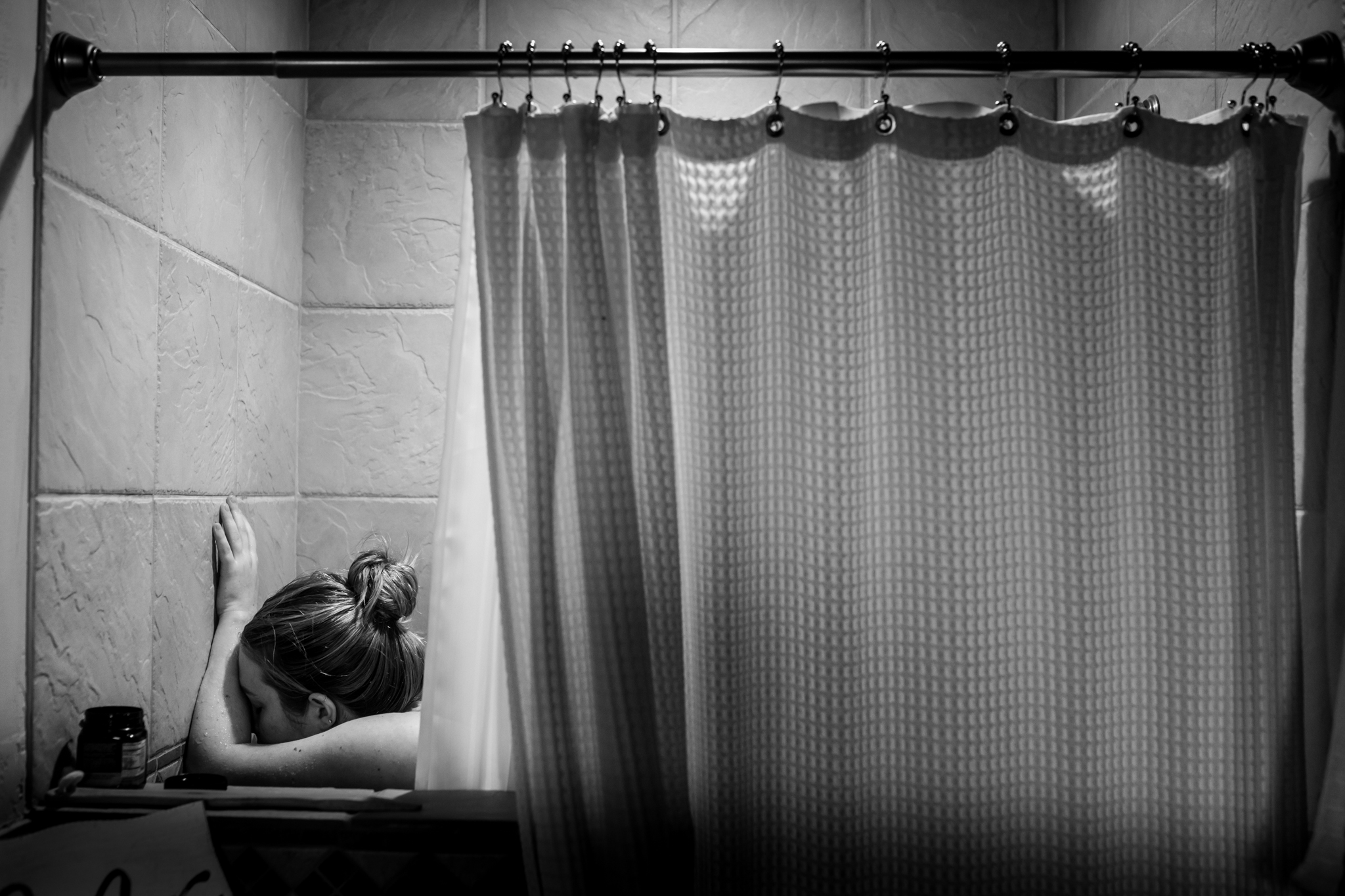 Lawren Rose Photography, a richardson texas birth photographer, takes a photo of a laboring mom utilizing the shower as a way to get through contractions during a home birth