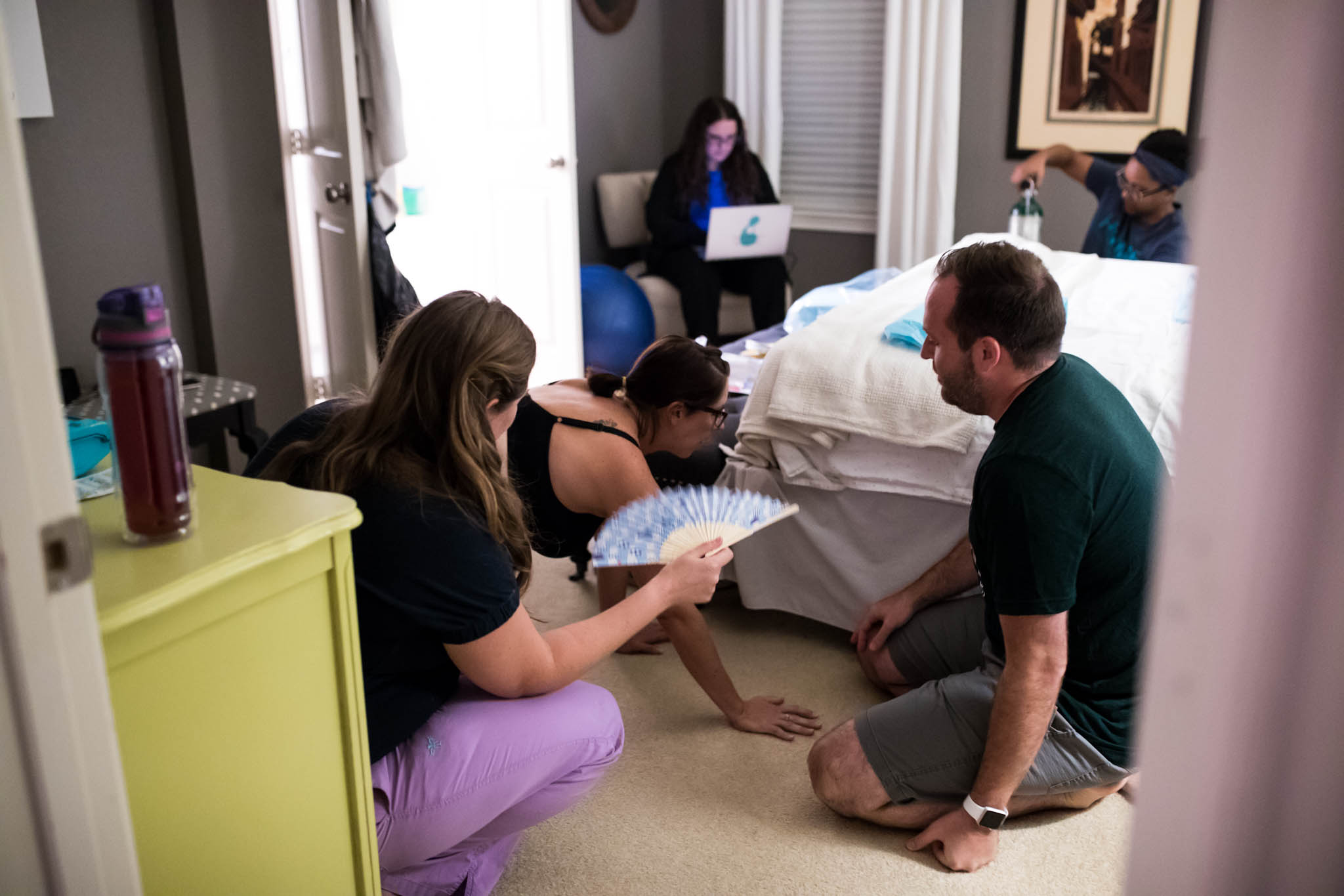 Lawren Rose Photography a DFW Birth Photographer takes an image peeking into the bedroom during a home birth in Denton, Texas as a laboring mom and the birth team are there watching and supporting her