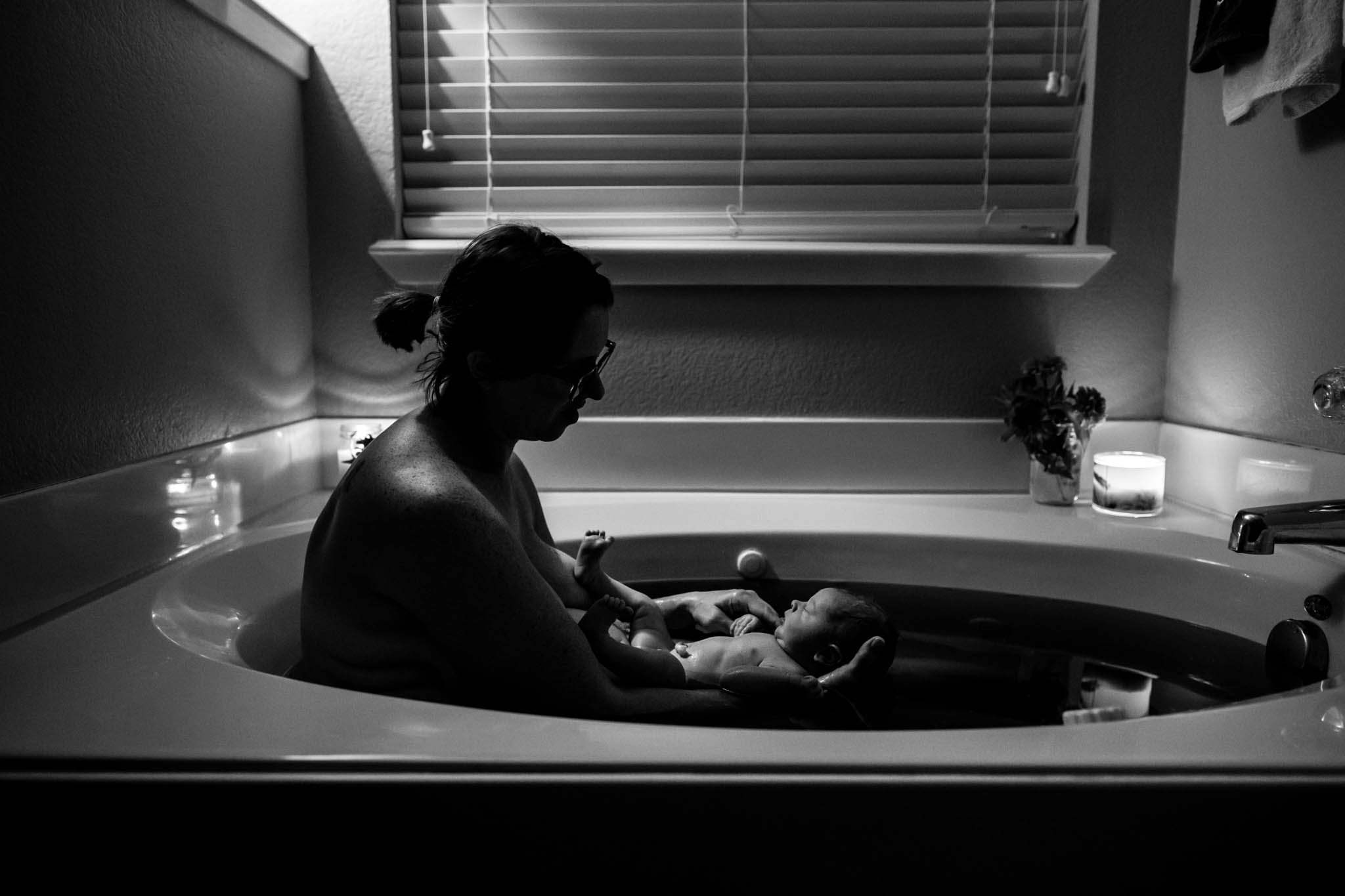 Lawren Rose Photography captures a moment during a candlelit herbal bath as Mom gets to check out her new baby boy born at home